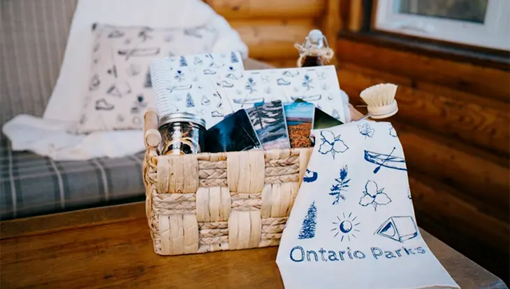 Plusieurs idées-cadeaux sur le thème des parcs de l’Ontario présentées dans un panier, dont une serviette, un carnet et un oreiller.