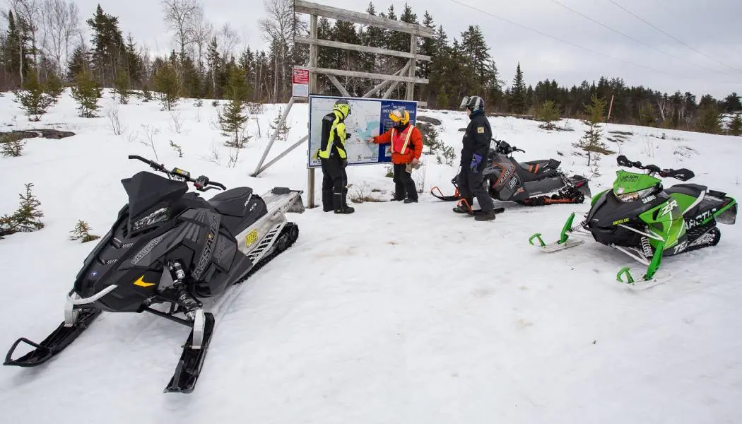 Snowmobilers checking a trail map kiosk beside their parked snowmobiles in New Liskeard.