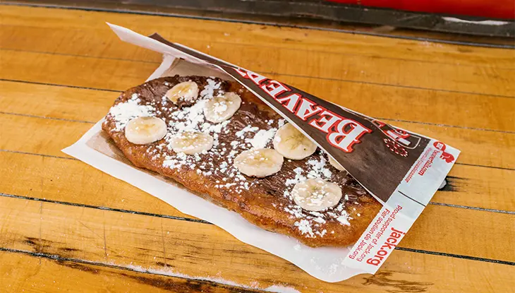 Pâtisserie queue de castor avec tartinade chocolatée, tranches de banane et sucre en poudre sur un comptoir en bois à Ottawa.