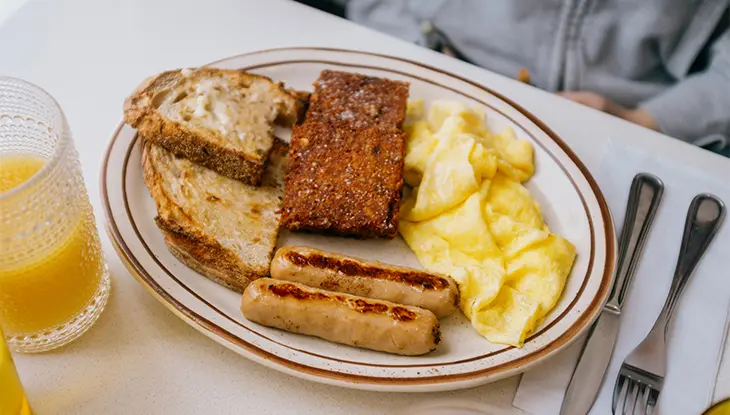 Assiette de déjeuner composée d’œufs, de rôties et de saucisses, accompagnée d’une tasse de jus d’orange, au restaurant DUKES à Ottawa.