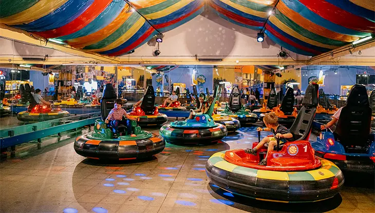 オタワにある屋内遊園地の、縞模様の天井照明の下で、人々がカラフルなバンパーカーに乗って楽しんでいる。