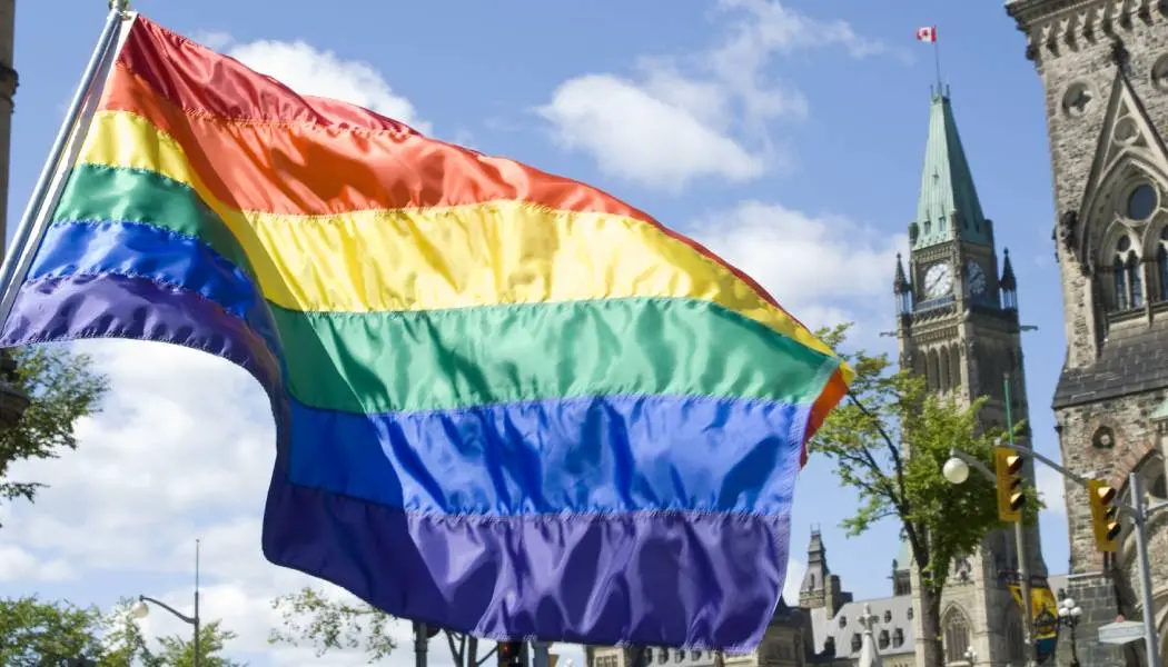 Drapeau arc-en-ciel hissé devant les bâtiments historiques du Parlement durant une célébration de la Fierté au centre-ville d’Ottawa.