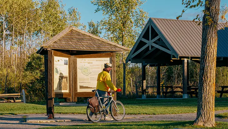 Un ciclista se detiene cerca de un panel informativo y un pabellón de picnic en Shirley’s Bay, en Ottawa.