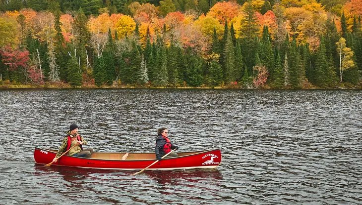 Deux personnes pagayant à bord d’un canot rouge sur un lac entouré de feuillage d’automne.