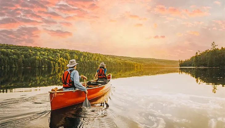 Deux personnes faisant du canot sur un lac calme au coucher du soleil.