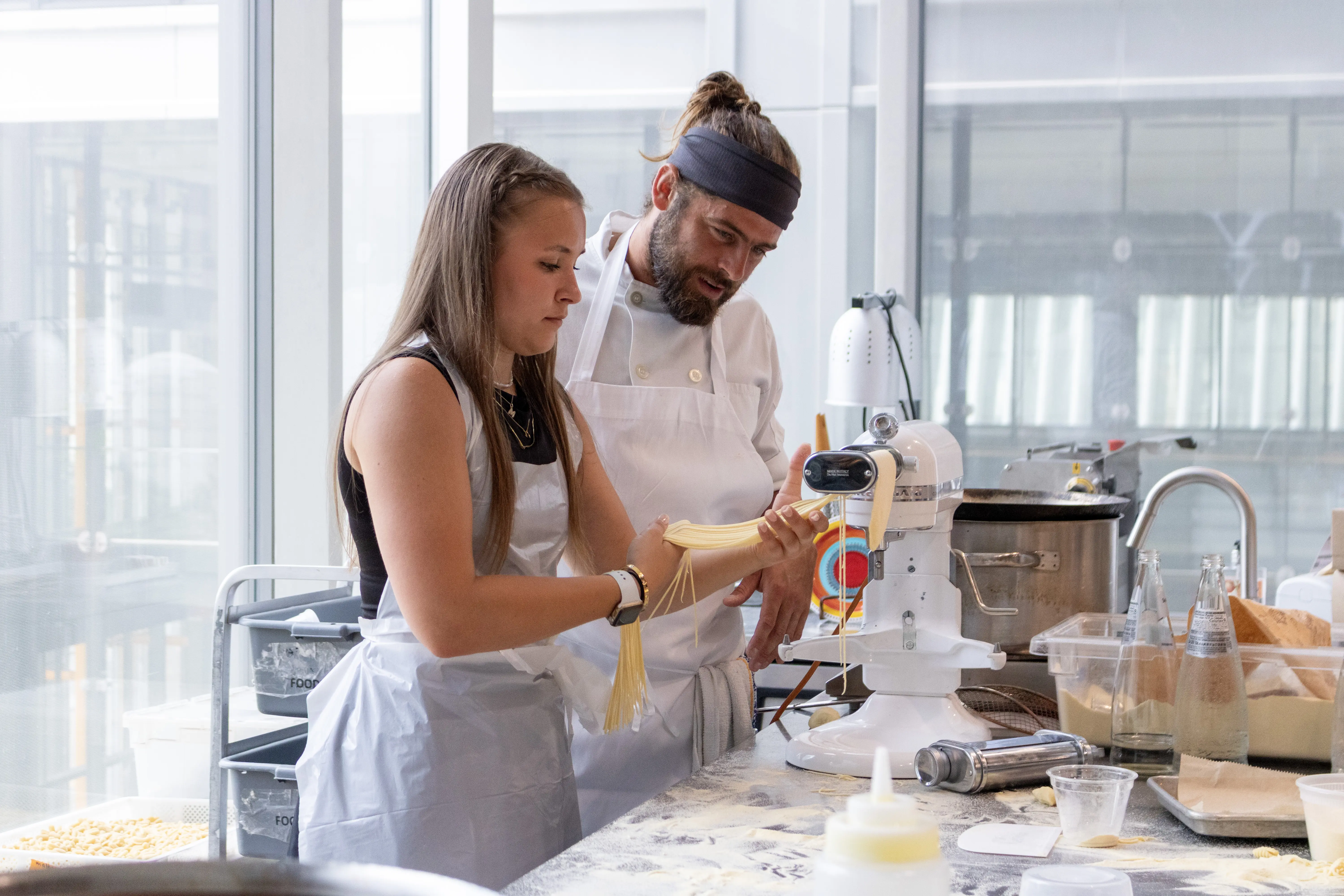 Chef observant une étudiante en cuisine couper des pâtes fraîches dans une machine.