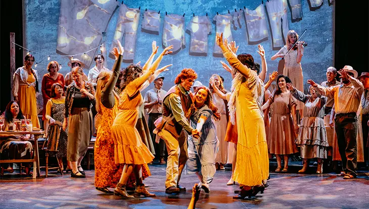 Performers dancing together on a brightly lit stage during a theatrical production.