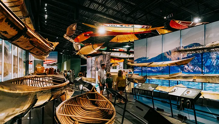 Canoes displayed in a museum gallery with visitors walking through.