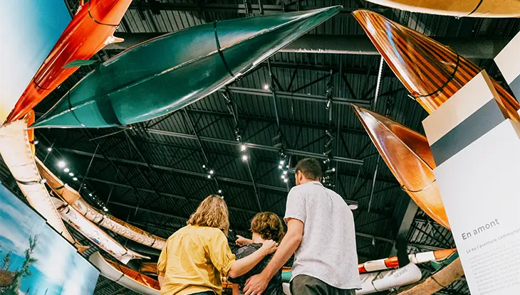 Une famille de trois personnes admire une exposition d'embarcations traditionnelles et modernes au Musée canadien du canoë.
