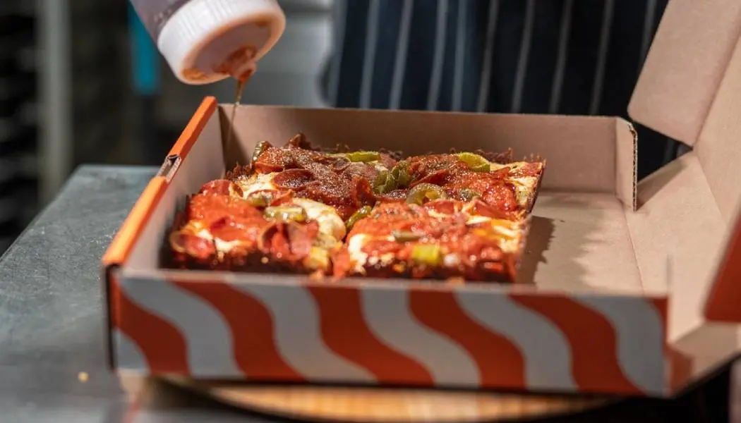 Des tranches de pizza fraîches dans une boîte à emporter sont garnies d’une sauce spéciale.