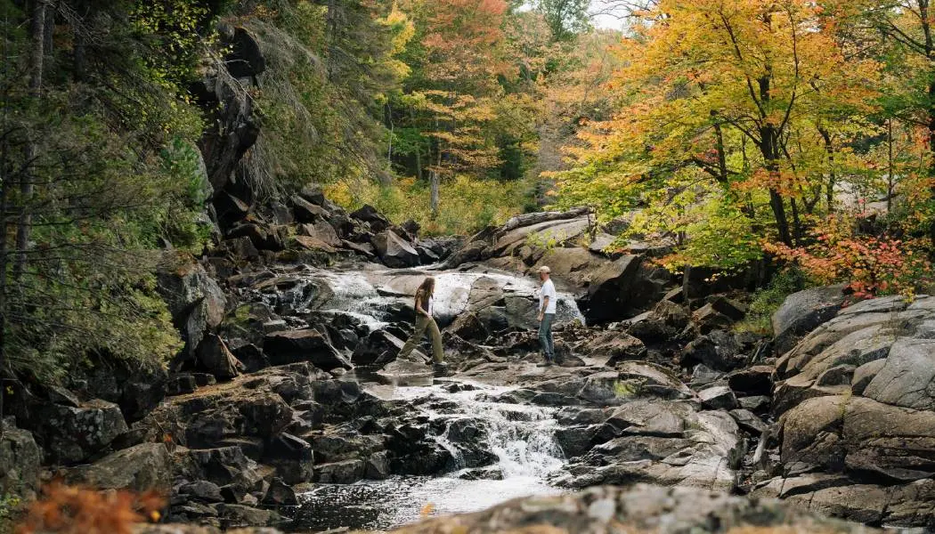 Deux personnes randonnent sur une cascade rocheuse entourée d'une forêt aux couleurs automnales flamboyantes dans le nord-est de l'Ontario.