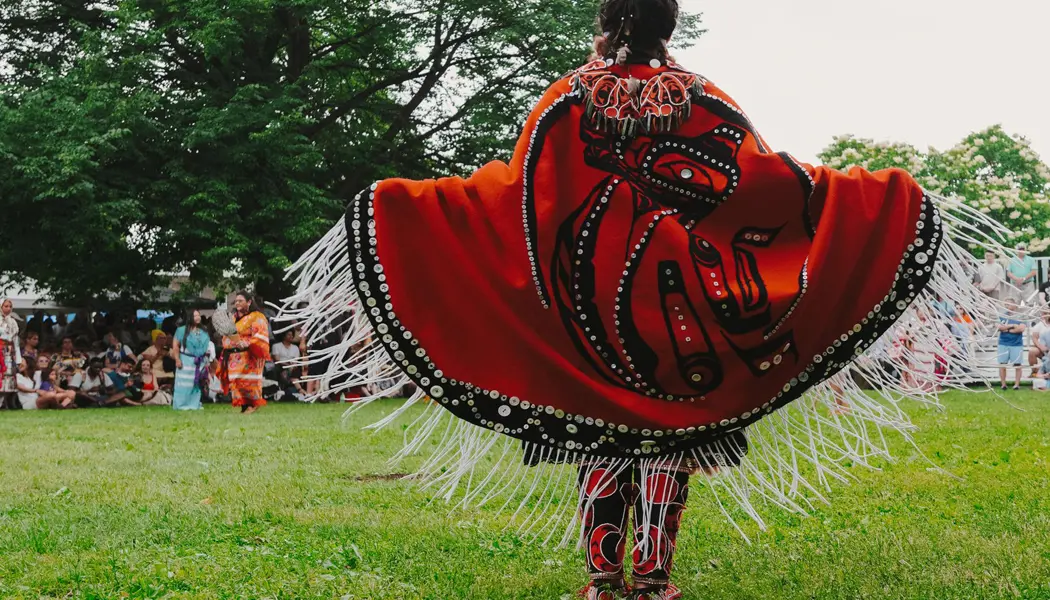 Eine indigene Tänzerin in einem reich verzierten rot-schwarzen Gewand tritt bei einer Zeremonie auf.