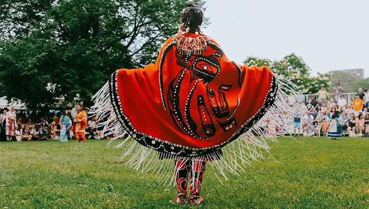 Danseur autochtone portant une cape à ornements rouges et noirs qui procède à une cérémonie