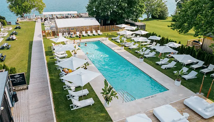 Außenpool umgeben von Liegestühlen und Sonnenschirmen in einem Seehotel mit Wasser im Hintergrund.
