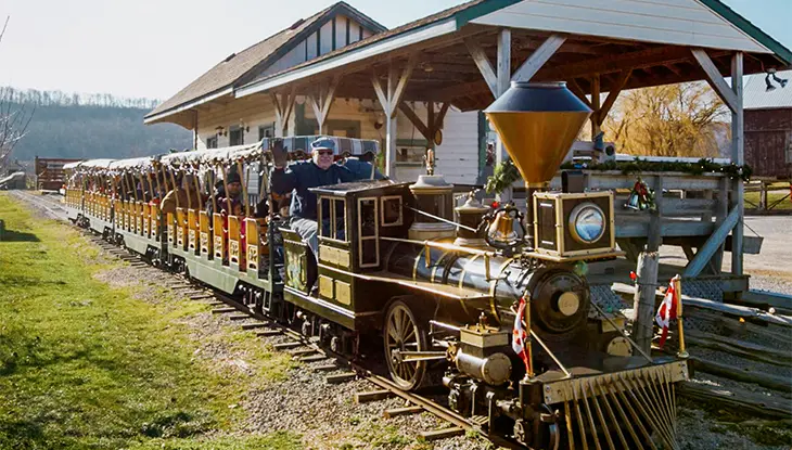 Petite locomotive arrêtée à une gare miniature, avec des passagers qui montent à bord avant le départ.