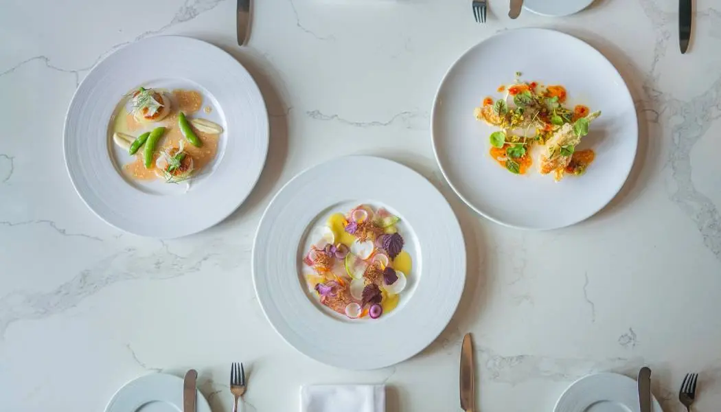 Table dressée dans un restaurant gastronomique, avec des mets colorés servis dans de la vaisselle blanche.