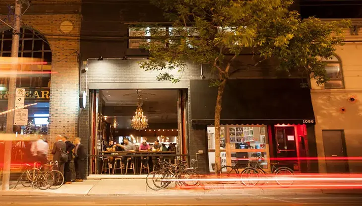 Des gens assis à un bar, regardant la rue. Des traînées de lumière rouge sont visibles.
