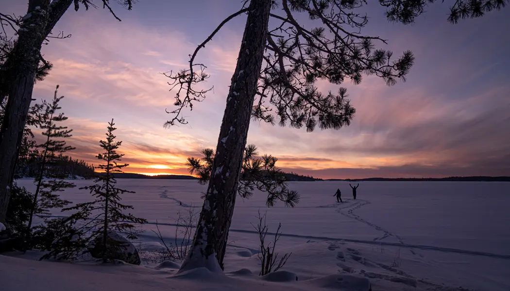 Ein Paar wandert in der Abenddämmerung mit Schneeschuhen über einen zugefrorenen See im Quetico Provincial Park.