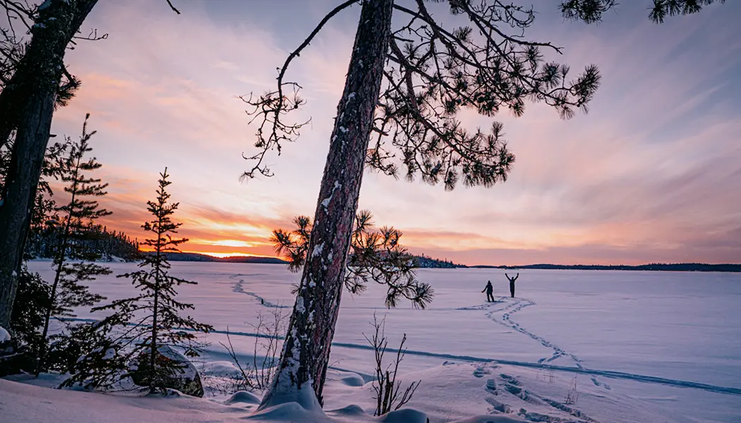 A couple snowshoeing across a frozen lake at dusk in Quetico Provincial Park.