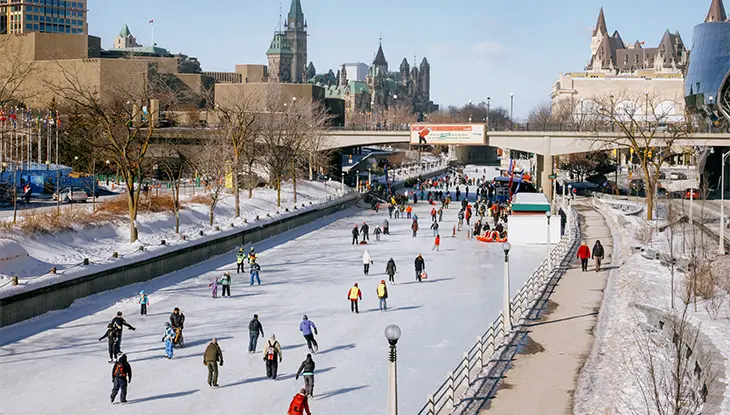 Patinaje diurno a lo largo del Canal Rideau en Ottawa con los edificios del Parlamento al fondo.