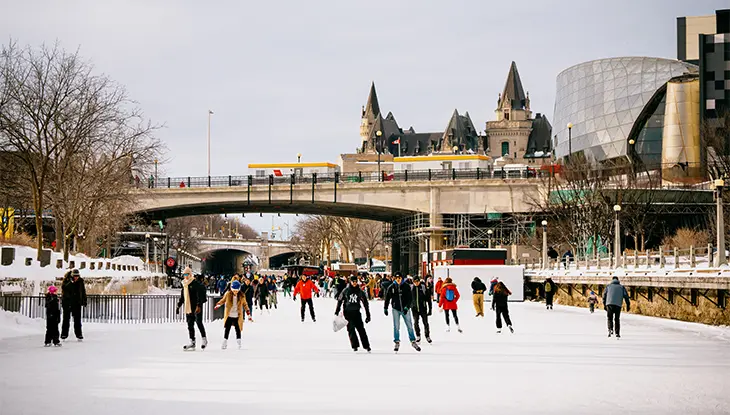 Gens patinant sur le canal Rideau gelé à Ottawa, avec les ponts, les bâtiments et le Fairmont Château Laurier en arrière-plan.