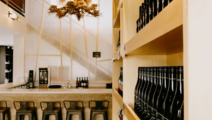 An empty bar with black chairs featuring a wine case with rows of black bottles sitting on shelves