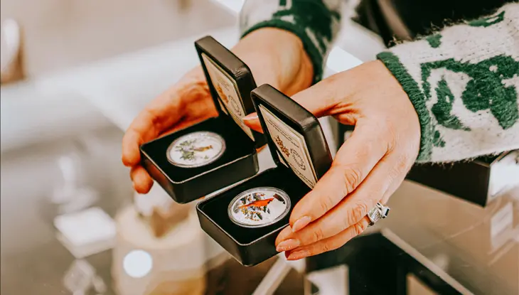 Hands holding two small Canadian Mint coins in black packaging inside a shop.
