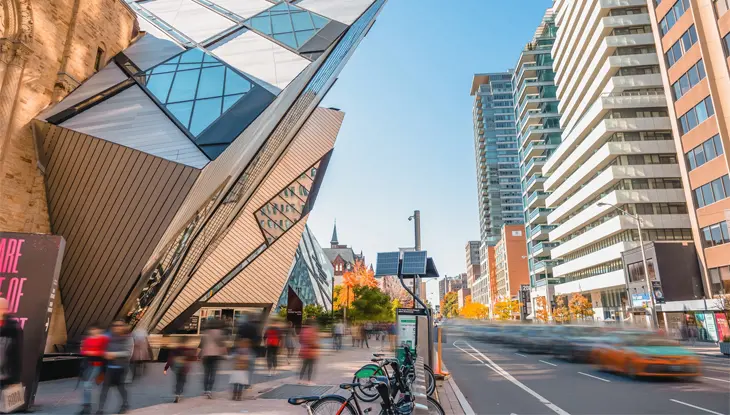 The iconic Royal Ontario Museum and other buildings line a bustling downtown Toronto street.
