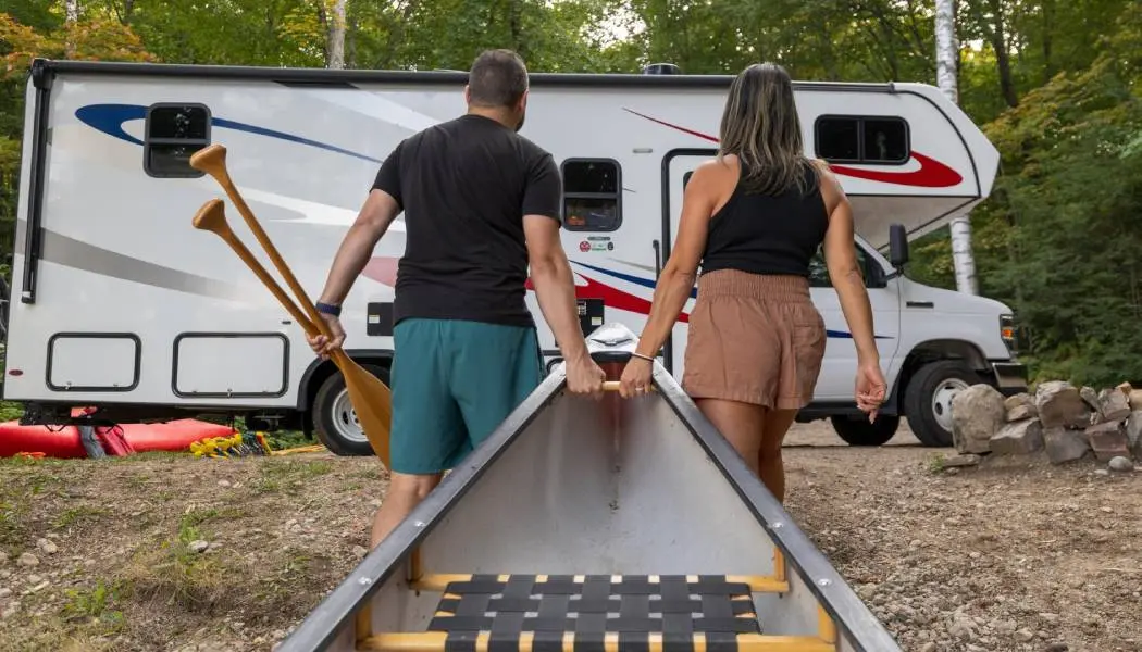 Ein Mann und eine Frau ziehen gemeinsam ein Kanu aus dem Wasser zu einem geparkten Wohnmobil.