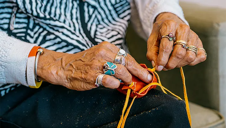 Close-up of hands wearing silver and turquoise rings sewing a handmade leather craft during an Indigenous cultural gathering in Sault Ste. Marie.