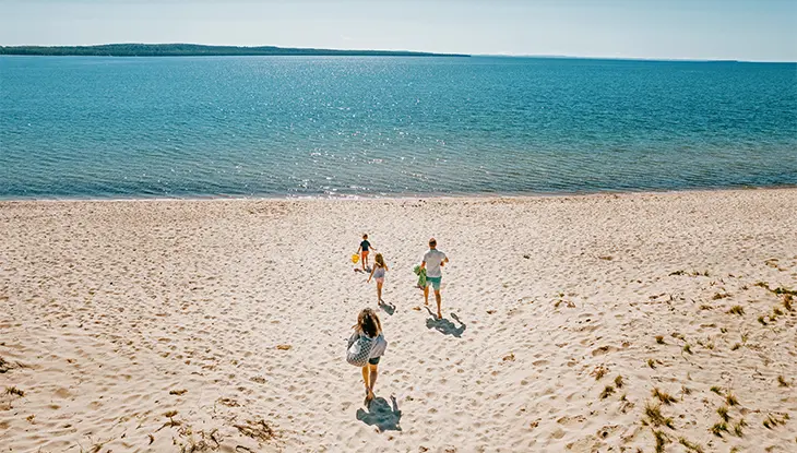 Family running down a sandy beach toward the water on a sunny day.