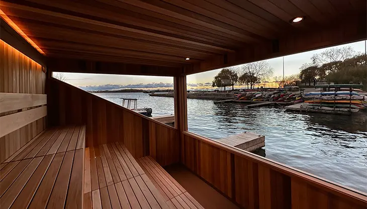Sauna en bois donnant sur une piscine thermale extérieure près de l’eau.