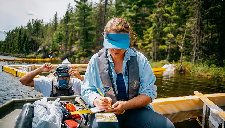 A researcher writes notes on a sustainable fishing study from a boat on a like.