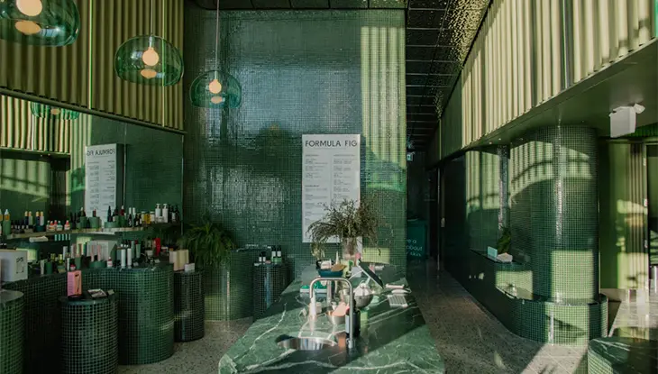 Intérieur d’une clinique de soins de la peau moderne avec des espaces de traitement, des présentoirs de produits et des ornements en verre vert.