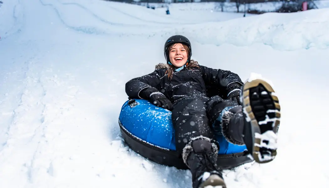 A teenage girl sitting in a blue inner tube slides down a snowy hill at Boler Mountain in London.