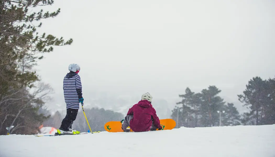 Deux planchistes se reposent au sommet d'une colline enneigée au parc de ski Laurentian à North Bay.
