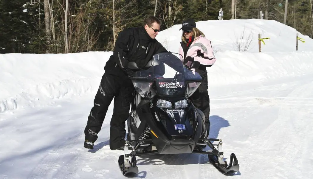 Instructor showing a first-time rider the controls of a rental snowmobile.