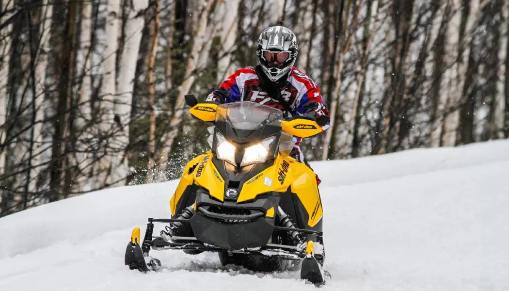 Family riding snowmobiles together on a groomed trail, yellow snowmobile leading.