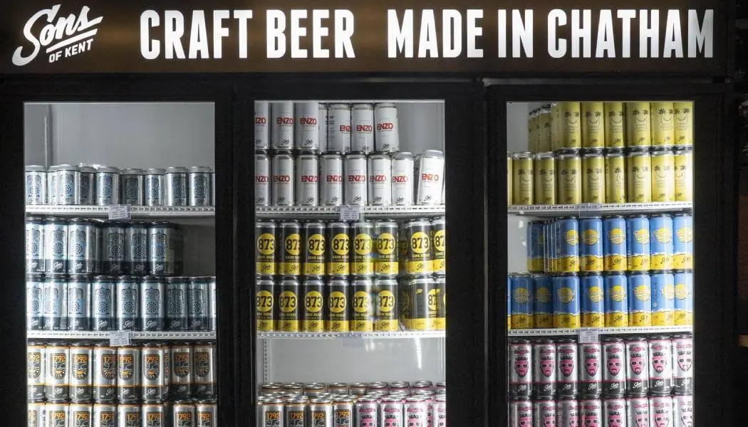 Rows of craft beer cans are stacked neatly in a fridge for take-away sale at a craft brewery.