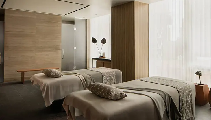 Salle de soins de spa comprenant deux lits de massage, un éclairage doux et des finis de bois neutres.