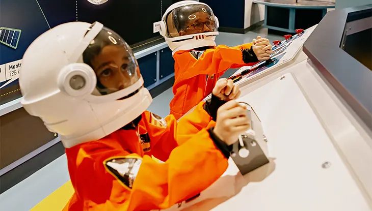 宇宙ヘルメットをかぶった子供が博物館内のインタラクティブな科学展示を楽しんでいます。