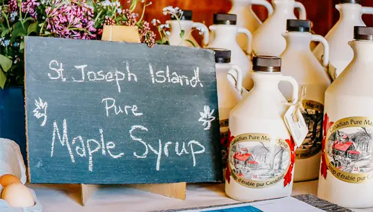 Display of St. Joseph Island pure maple syrup bottles with a chalkboard sign at the Maple Syrup Festival.