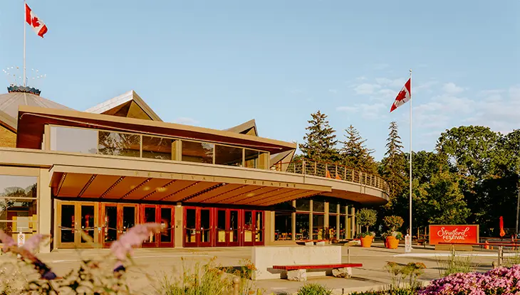 Theatre building entrance with Canadian flags and landscaped garden.