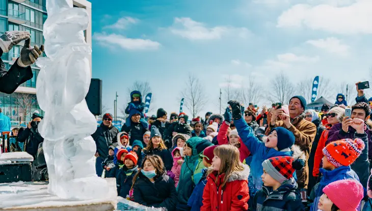 Ice carver shaping a sculpture as families and children watch during the Sugar Shack TO festival in winter.