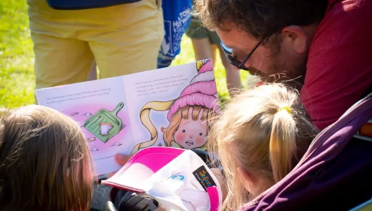 Ein Mann liest zwei Mädchen ein Buch vor
