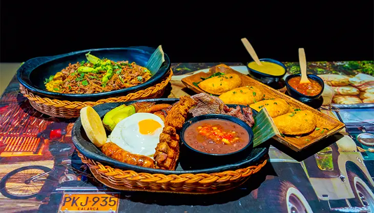 Person holding an oyster over a platter of fresh oysters with lemon, sauce, and a glass of sparkling wine.