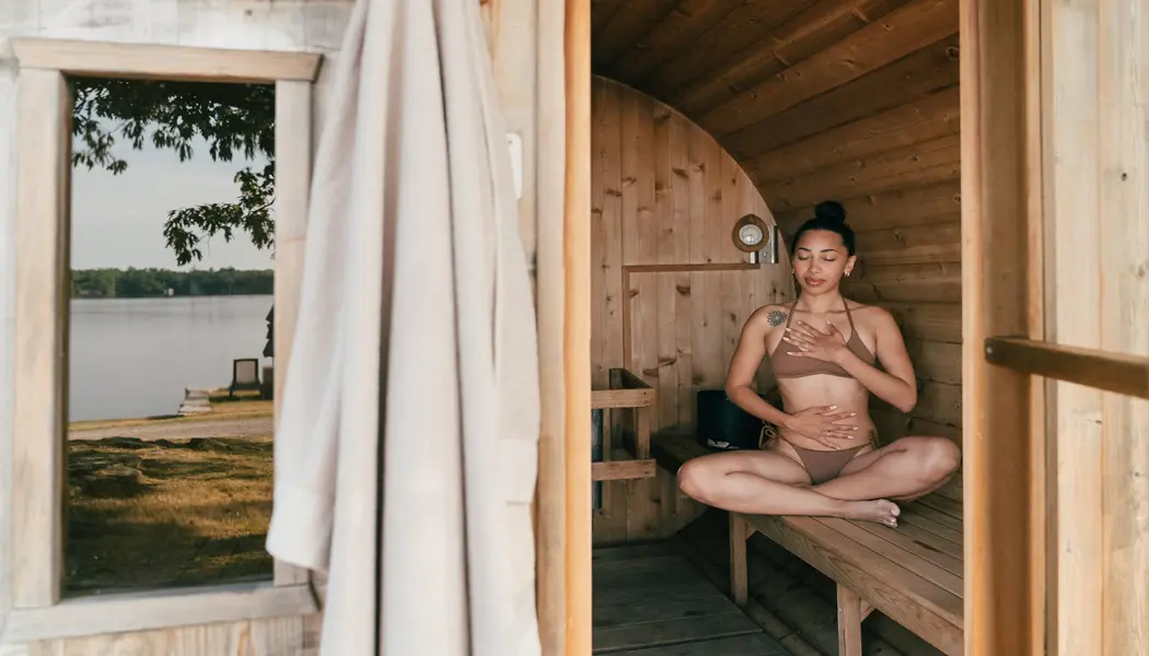 Una mujer joven se relaja en una sauna de madera con vistas a un pintoresco lago.