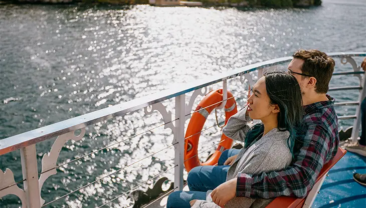 Zwei Personen sitzen auf einem Boot und genießen eine malerische Fahrt mit Wasser und Inseln im Hintergrund.