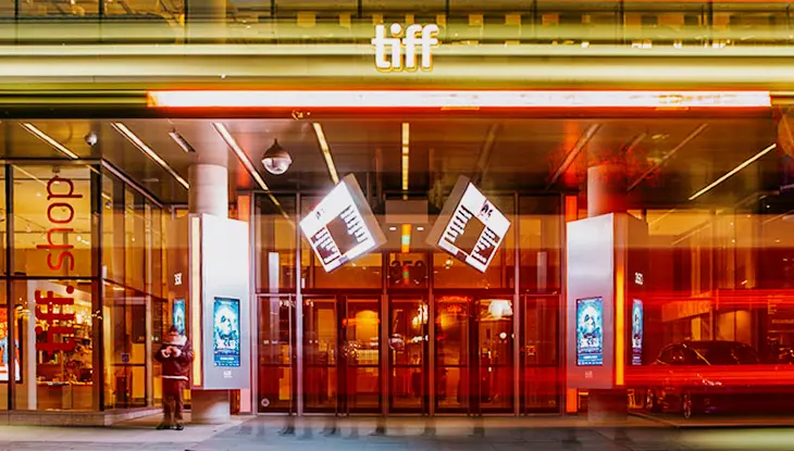 Entrada de cine con fachada de vidrio iluminada con letreros de neón brillantes por la noche.