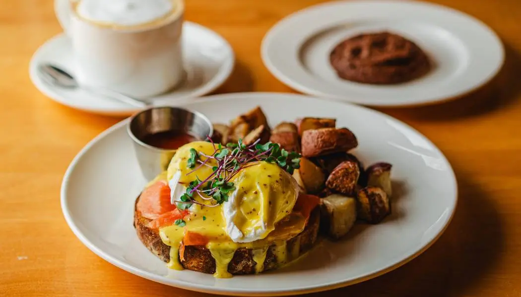 Une assiette de brunch composée d'œufs Bénédicte sur toast avec saumon fumé, pommes de terre rissolées et café.